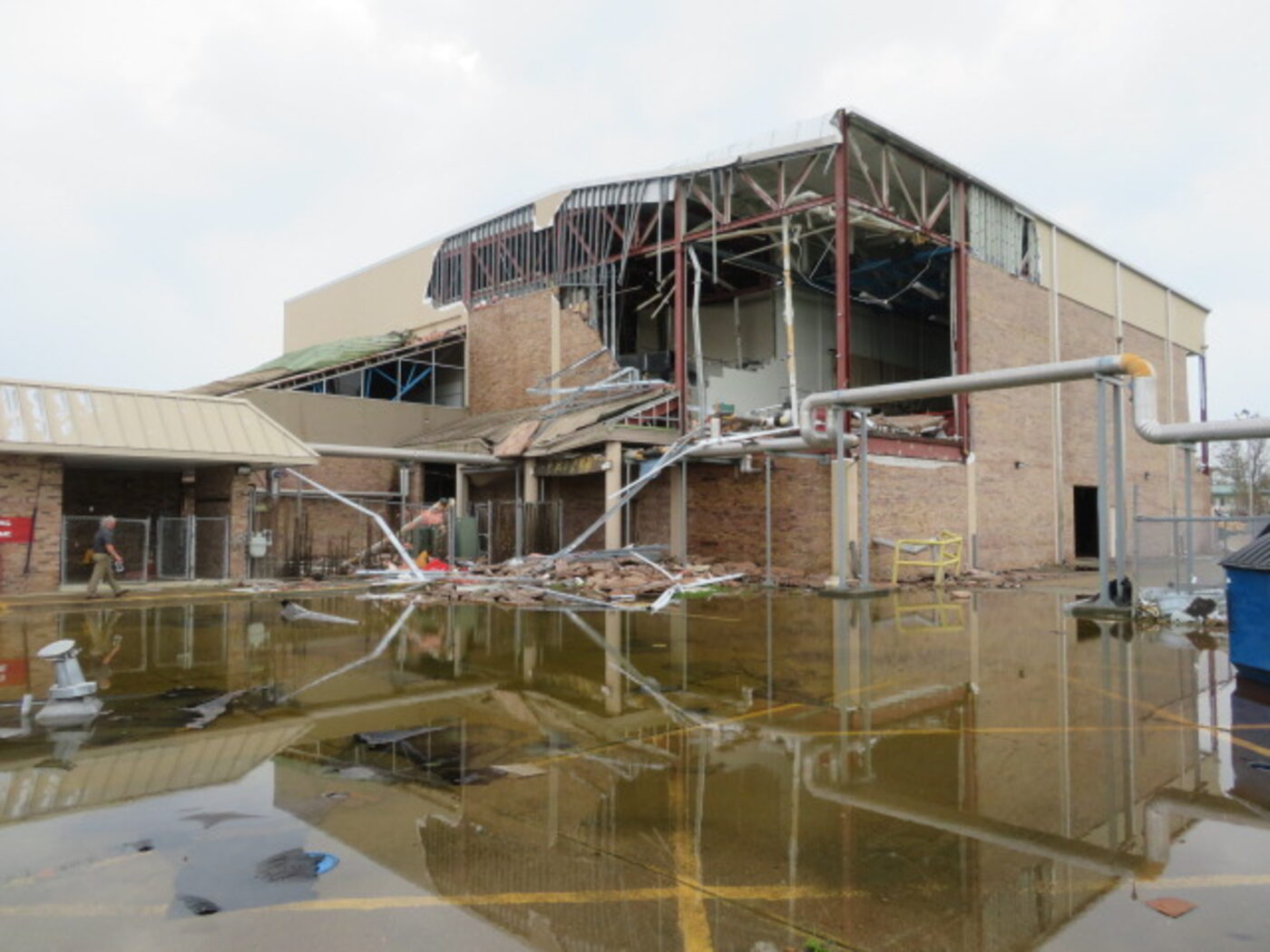 Collapsed gymnasium wall and standing water at a school campus after Hurricane Ida